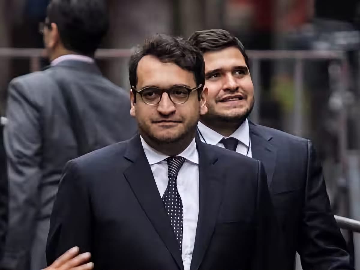 Hombre de traje y lentes caminando en entorno urbano